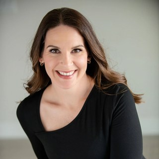 Adrienne Dorison, smiling brunette in a black top against a soft gray studio background