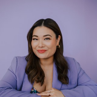 Ellen Yin, smiling with long brown hair in a lavender blazer against a matching lavender backdrop